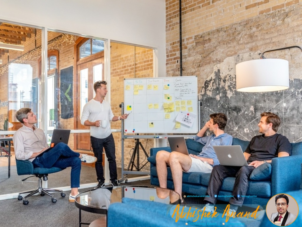 three men sitting while using laptops and watching man beside whiteboard