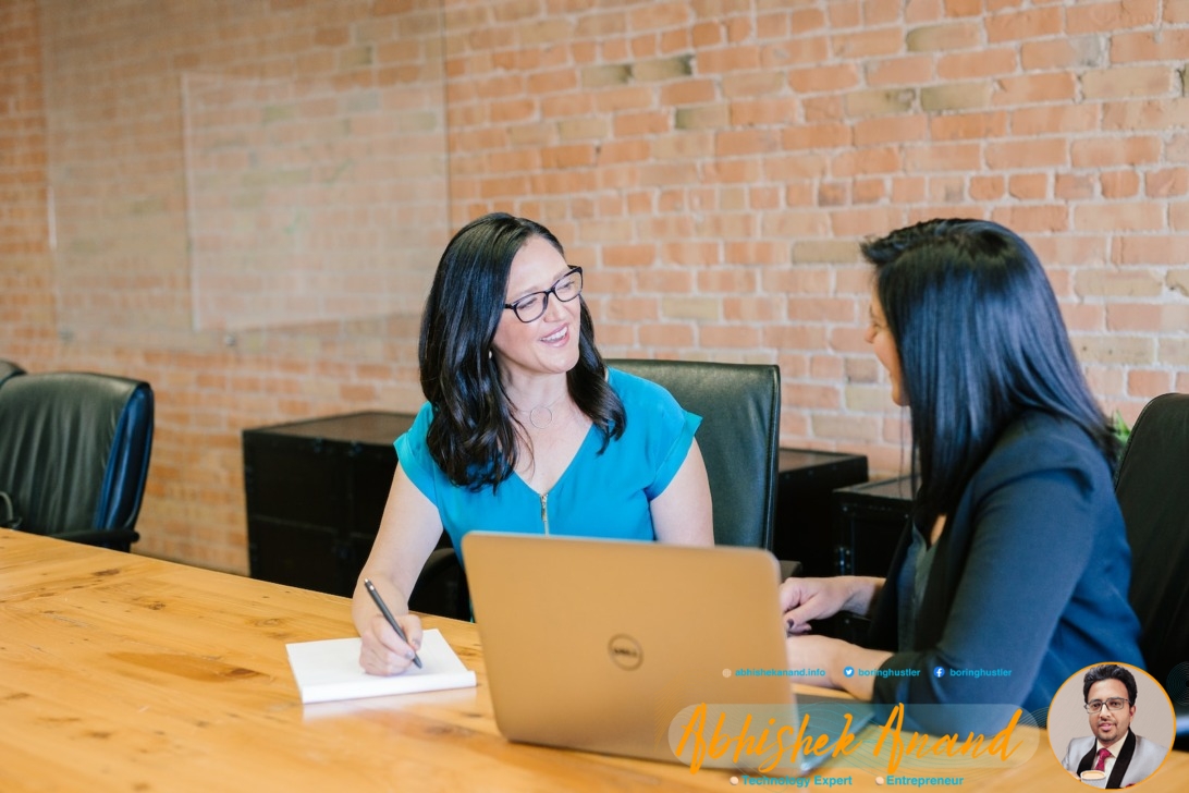 woman in teal t-shirt sitting beside woman in suit jacket